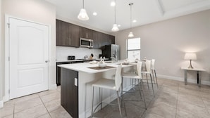 A modern kitchen with a central island, bar stools, and pendant lighting. - Balmoral Resort-222mcv 4 Bedroom Home by RedAwning (Haines City)