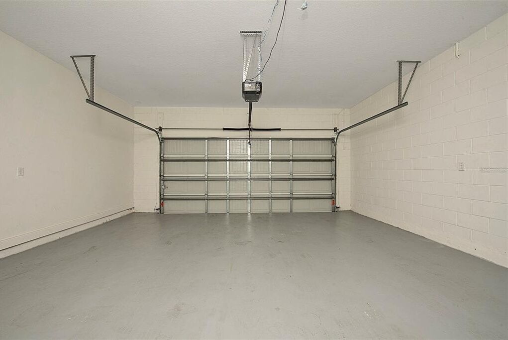 A garage with a closed garage door, a ceiling-mounted projector, and a plain white brick wall.