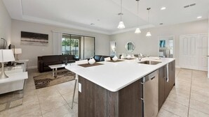 A modern kitchen with a central island, pendant lighting, and a view to the living area. - Balmoral Resort-222mcv 4 Bedroom Home by RedAwning (Haines City)