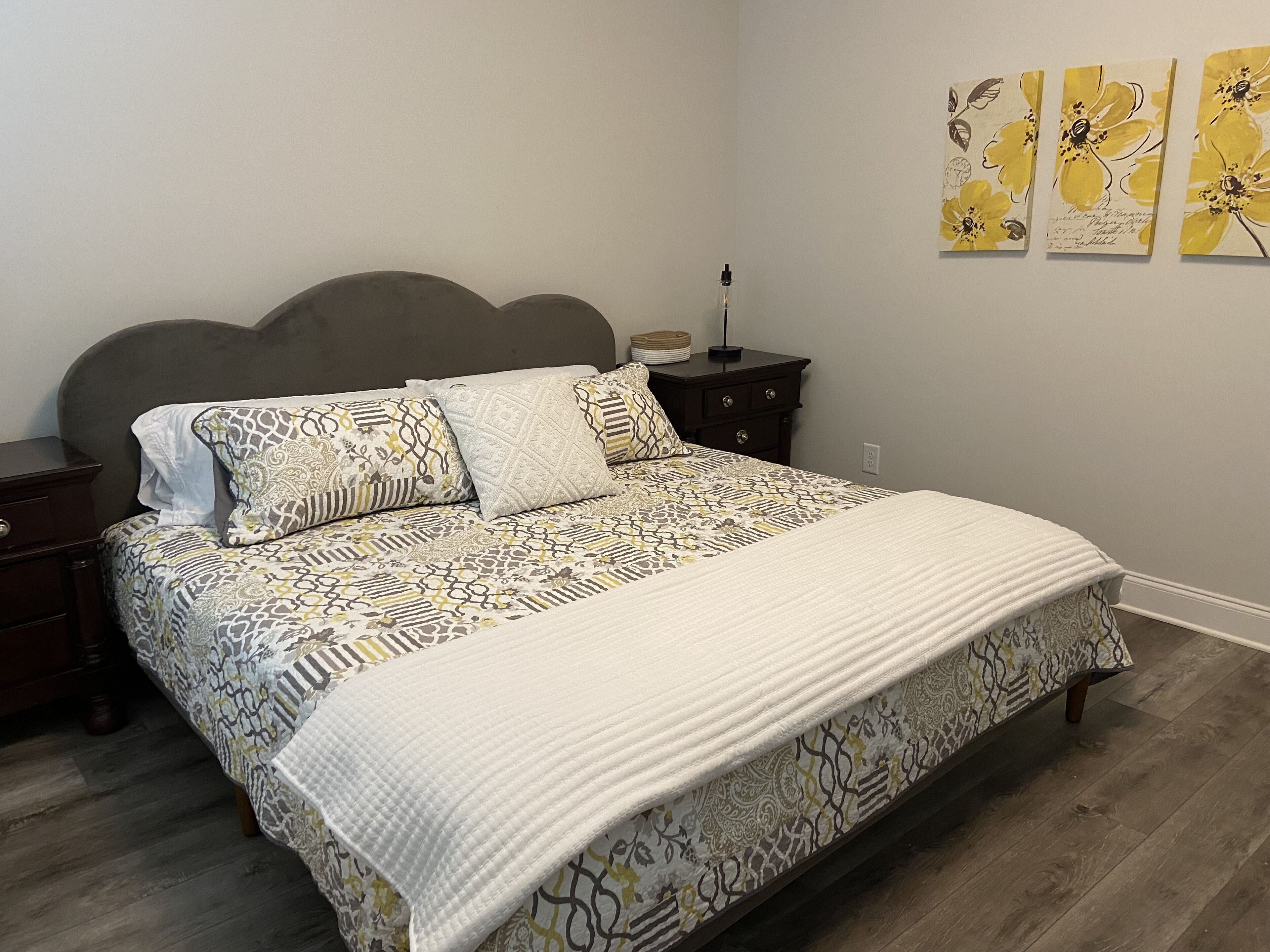 Une chambre à coucher comprenant un lit, une table de chevet, une commode et un mur orné de trois œuvres d’art encadrées.