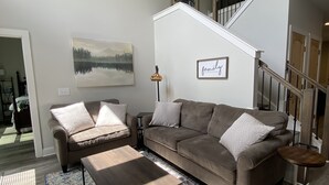 A spacious living room with a large sofa, a coffee table, and a patterned rug. A staircase leads to an upper level. - Downtown Clayton Townhouse (Clayton)