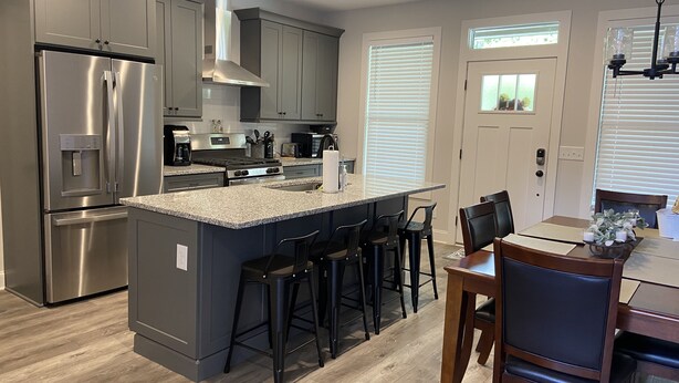 A modern kitchen with grey cabinetry, stainless steel appliances, and a central island with bar stools. - Downtown Clayton Townhouse (Clayton)