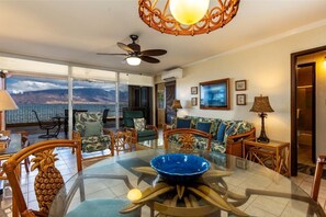 A room with a glass-top table, chairs, a ceiling fan, and a view of the ocean. - Menehune Shores, #210 3 Bedroom Condo by RedAwning (Kihei)