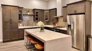 Una cocina moderna con armarios de madera oscura, un protector contra salpicaduras de piedra, un refrigerador de acero inoxidable e isla central con taburetes de bar.