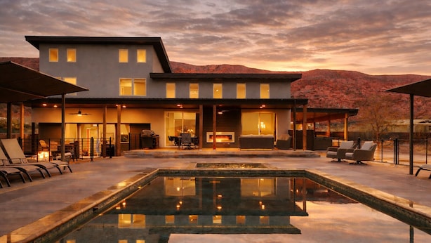 Una casa moderna de dos pisos con piscina, mobiliario exterior y chimenea.