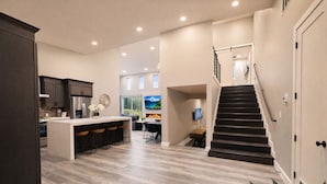 Una cocina moderna con una isla central, un comedor y una escalera que sube a un espacio tipo loft.