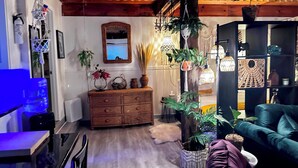 A cozy living room with a wooden ceiling, a blue sofa, a wooden cabinet, and various decorative items including plants and hanging lights.