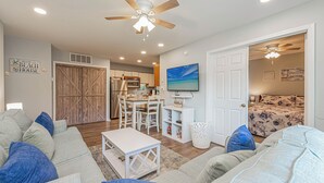 A living room with a sofa, a coffee table, a TV, and a ceiling fan. - Renovated 1st Fl 2BR/2BA, priv patio! Indoor/outdoor Pool; steps to BEACH & Dine (Ocean City)