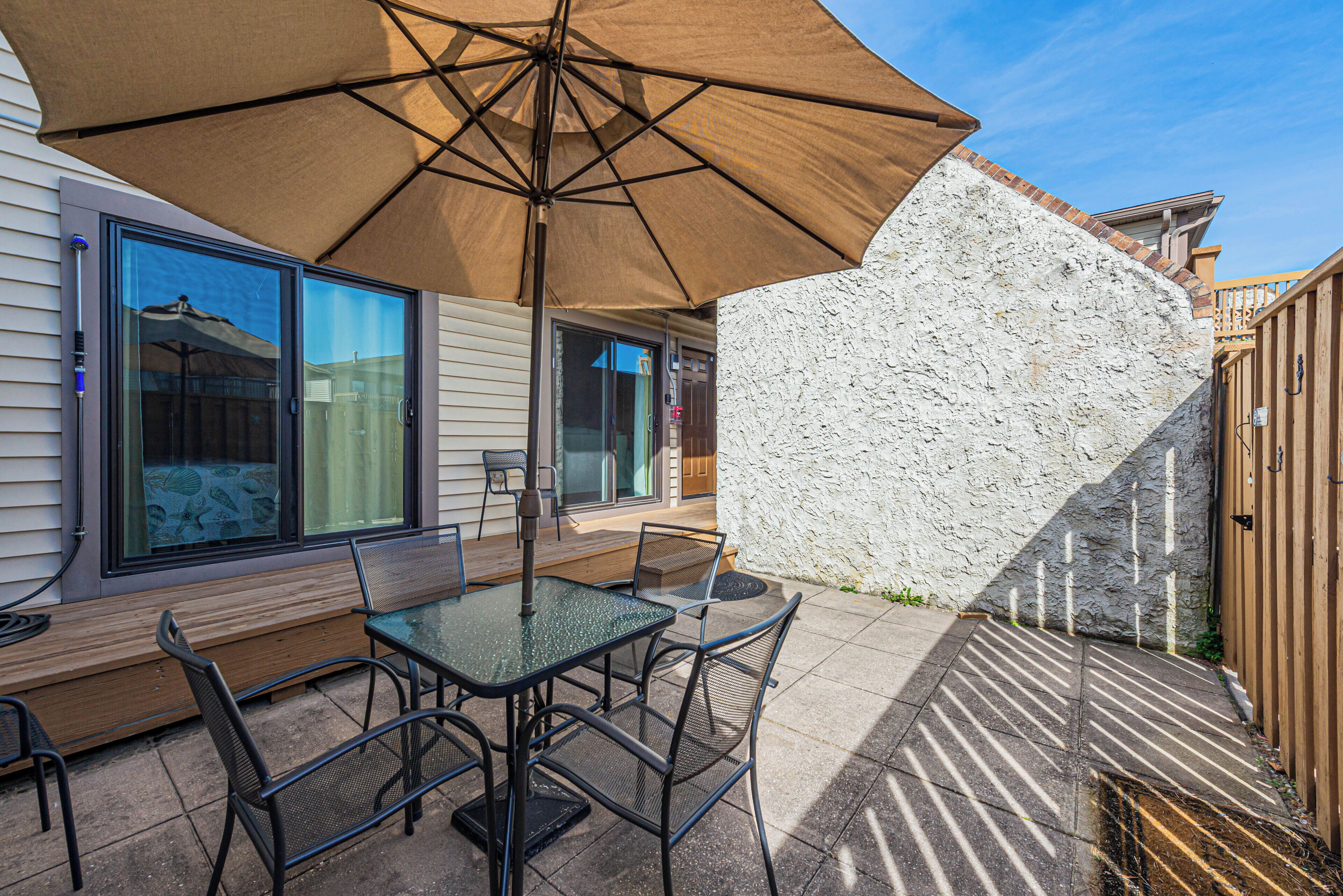 Een terras buiten, met een tafel, stoelen, een grote parasol en een stenen muur.