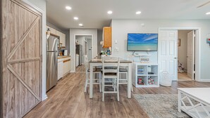 A modern kitchen with wooden cabinets, a dining area with white chairs, and a TV mounted on the wall. - Renovated 1st Fl 2BR/2BA, priv patio! Indoor/outdoor Pool; steps to BEACH & Dine (Ocean City)