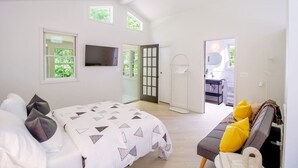 A bedroom with a bed, a TV, a sofa, and a bathroom visible through an open door.