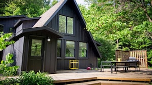 A modern house with a dark exterior, large windows, and a deck with outdoor furniture.