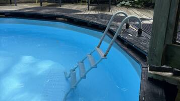 Una piscina con escalera, rodeada por una terraza de madera y sillas.