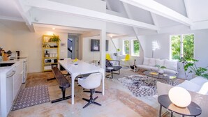A spacious living area with a white sofa, a dining table, and a kitchen area with a yellow shelf.