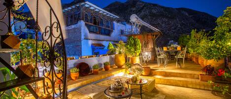 Un patio con mesas al aire libre, plantas en macetas y montañas al fondo.
