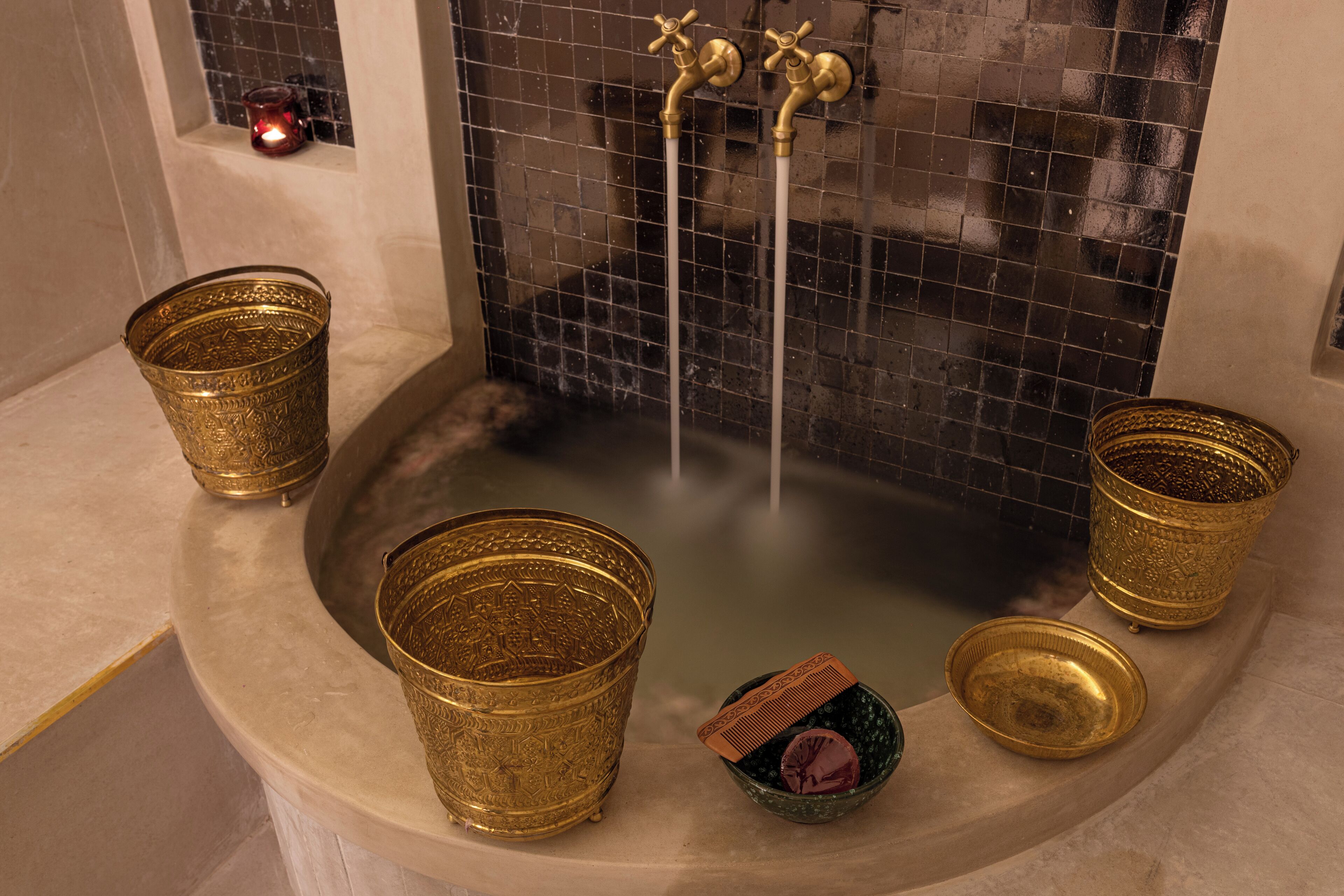 A bathtub with two faucets, a candle, and three ornate golden containers.