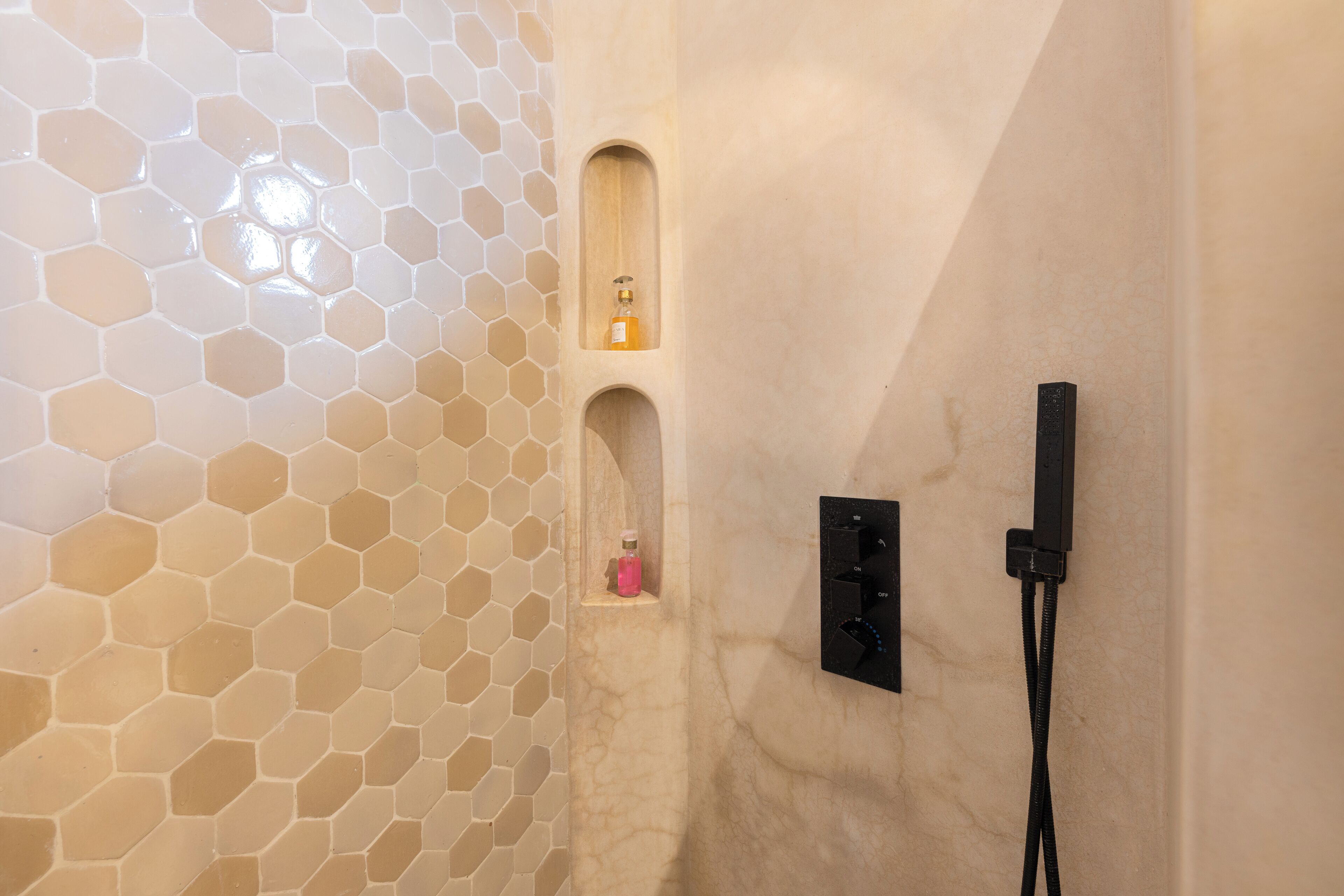 Un baño con paredes de azulejos hexagonales, una zona de ducha y dispensador de jabón empotrado.