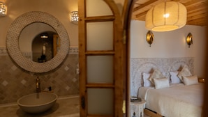 A bathroom with a round mirror, a wooden door, and a bed with patterned bedding.