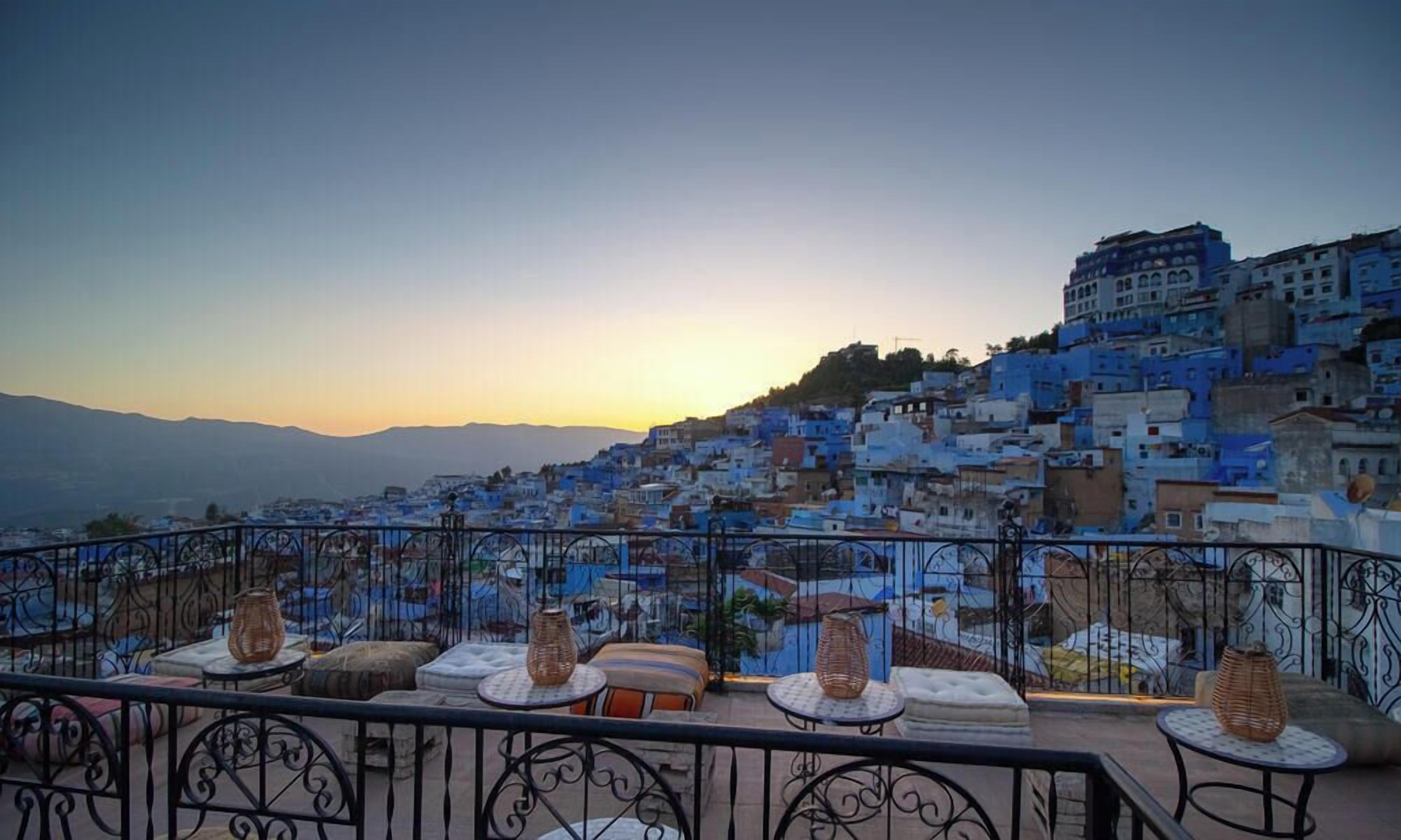 A terrace with outdoor seating and a view of a densely packed town with blue buildings.