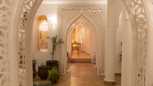 A corridor with intricate white lattice work, leading to a room with a wooden chair and a table.
