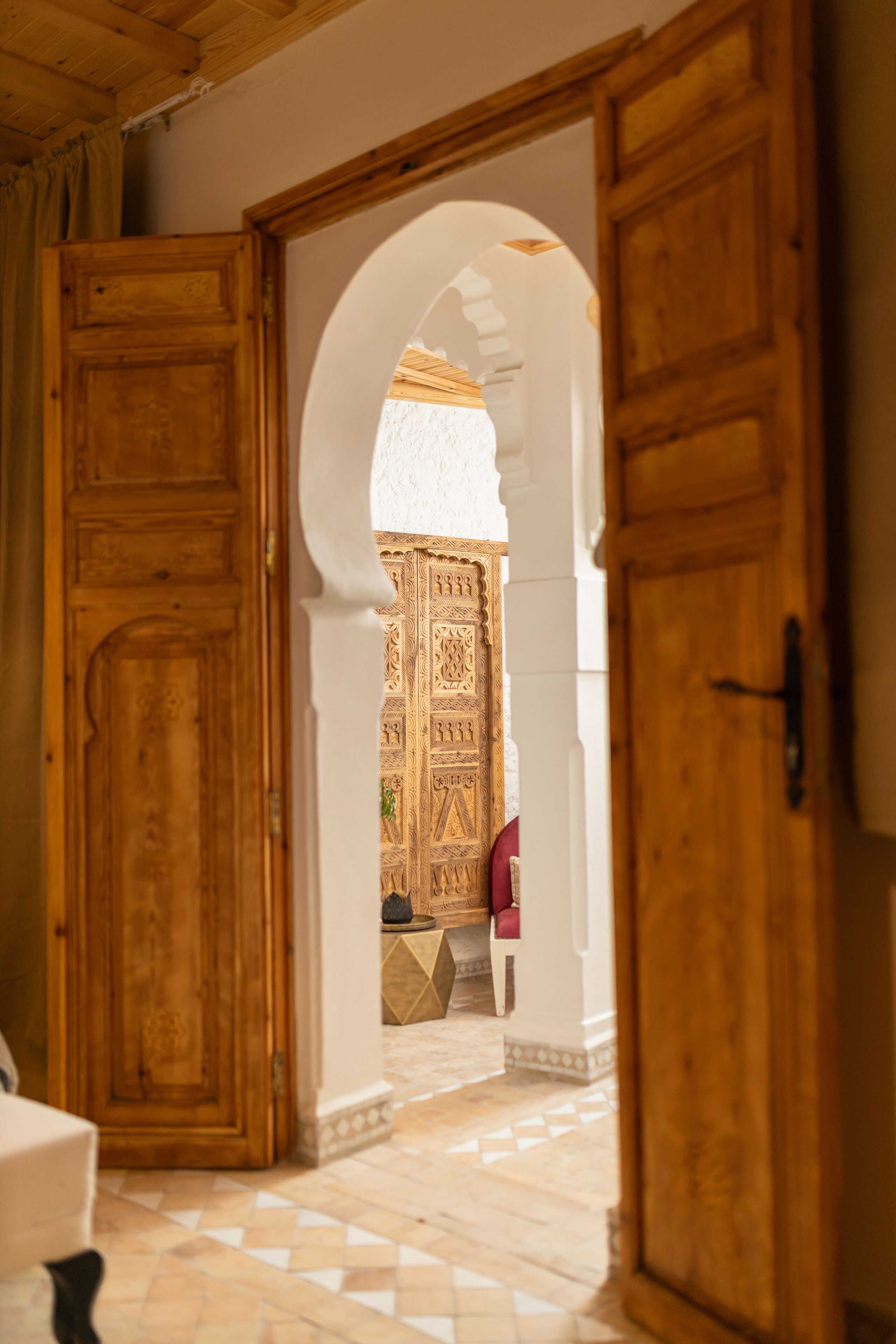 Un pasillo interior con puertas de madera, suelo de baldosas y un arco que conduce a una habitación con puerta decorada.