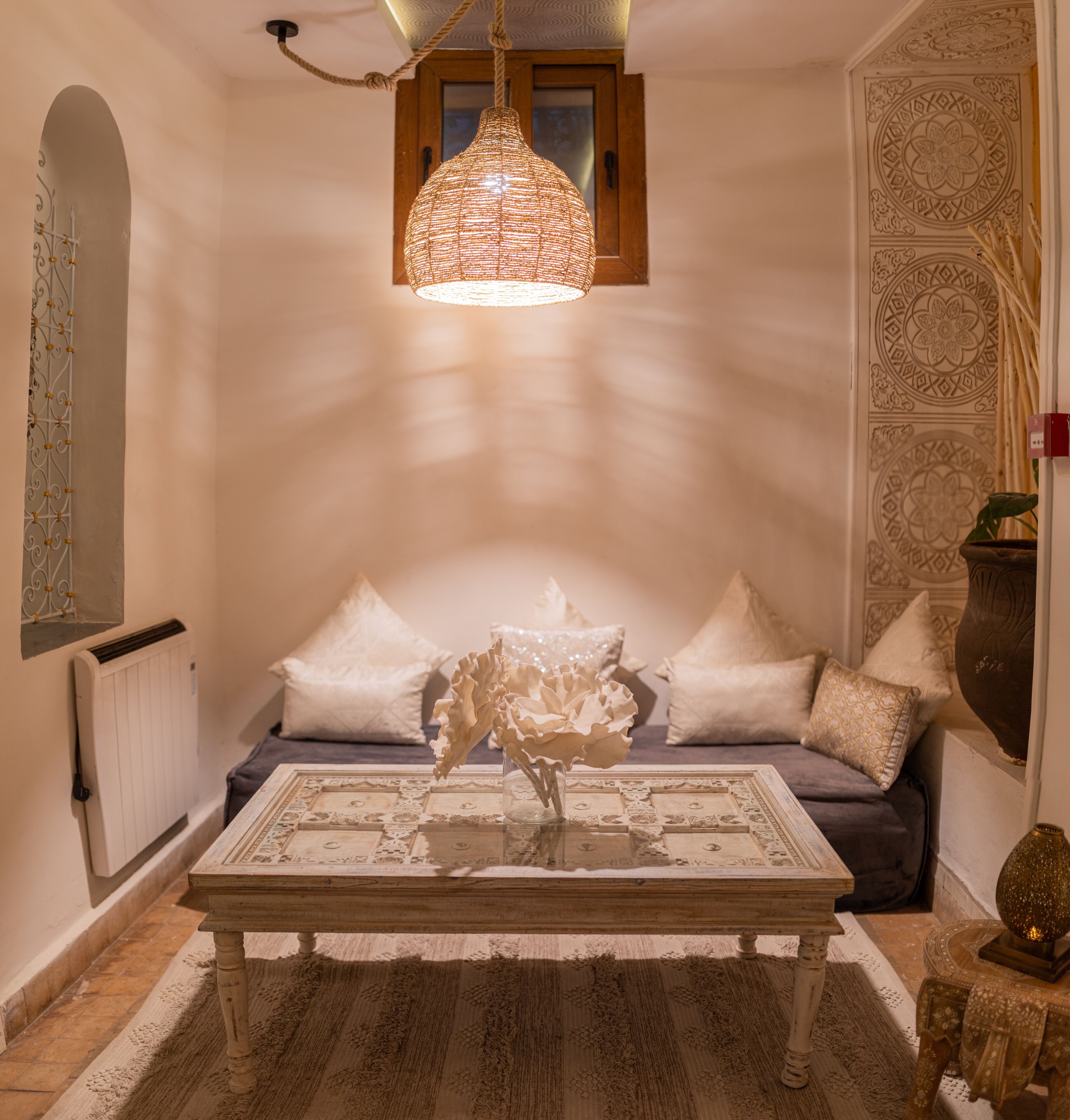 Un cuarto acogedor con una mesa de centro estampada, un sofá con cojines decorativos, una lámpara colgante y un panel de pared decorativo.