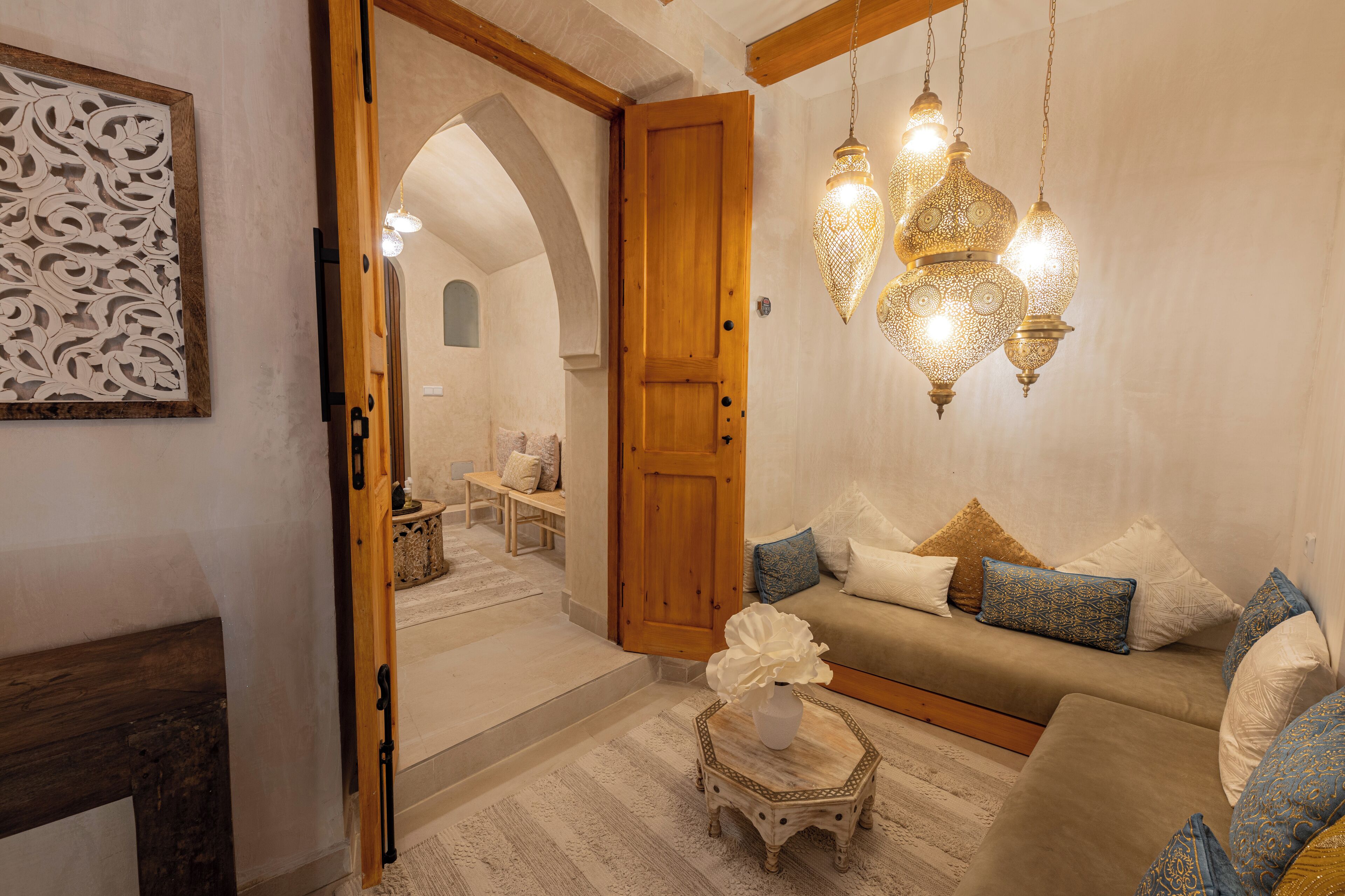 A cozy living room with a sofa, decorative pillows, a small table with a vase, and hanging lanterns.