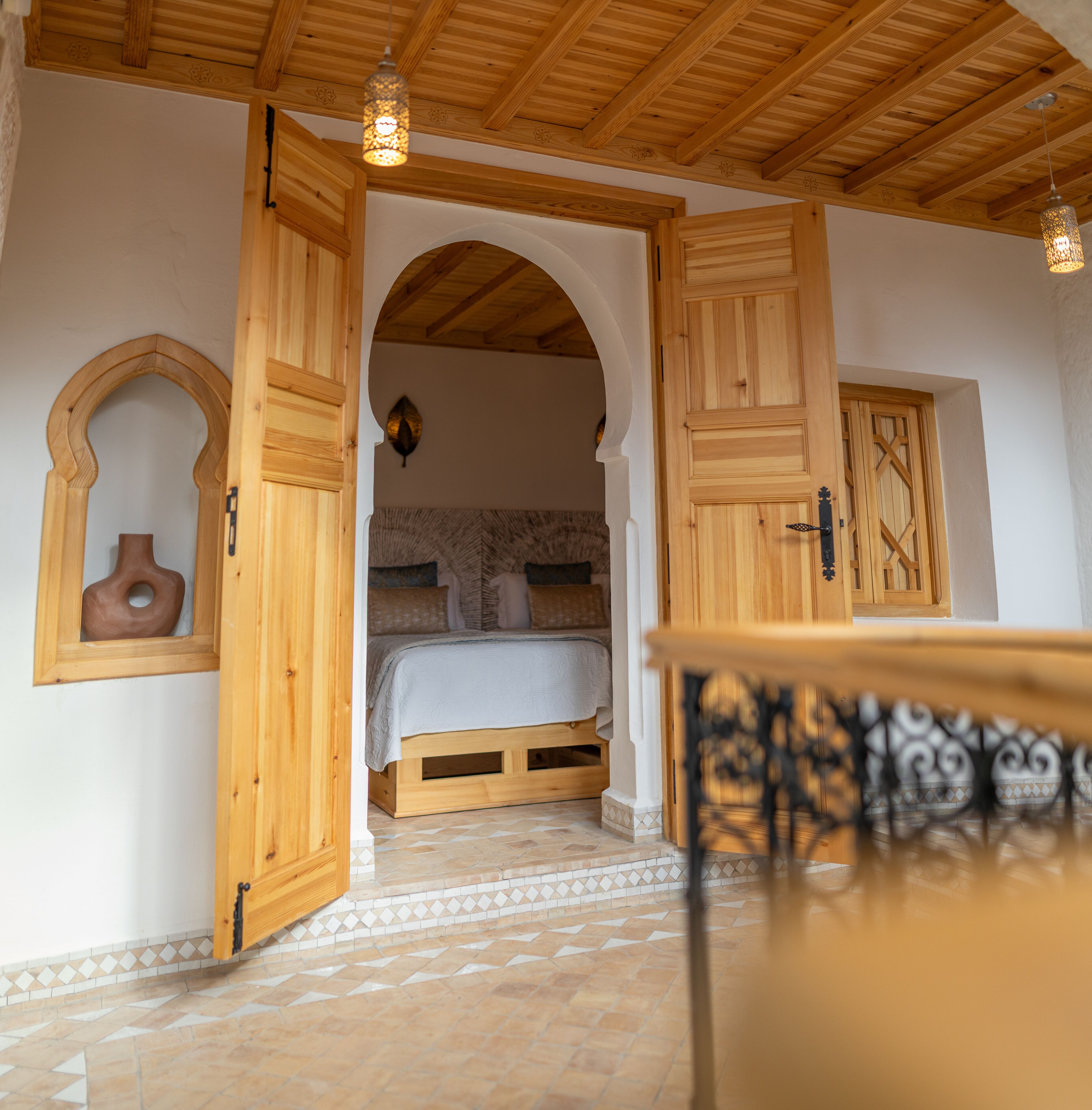 Una habitación con una cama, puertas de madera y suelo de baldosas.