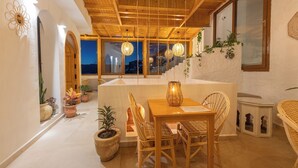 A cozy dining area with wooden furniture and potted plants, featuring a view of the city at dusk.