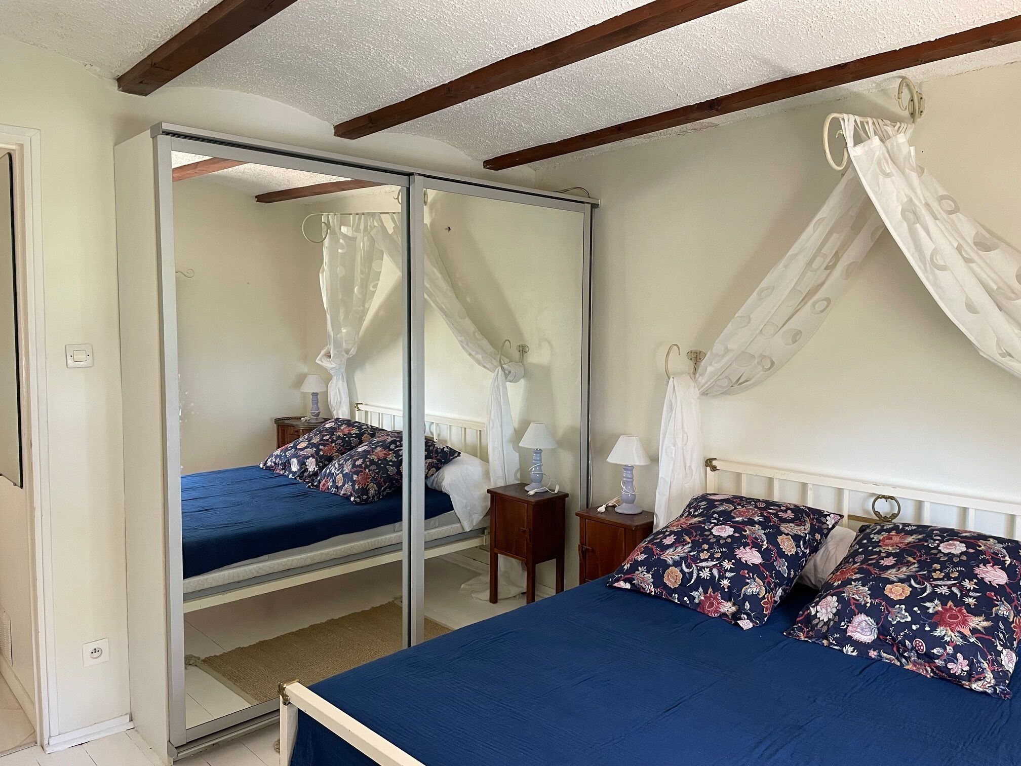 A bedroom with a mirrored wardrobe, a canopy bed, and a bedside table with a lamp.