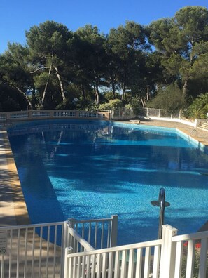 A rectangular swimming pool with a white deck and metal railing, surrounded by trees and a clear sky. - Appartement Dans Résidence de Standing à Hyeres (Hyères)