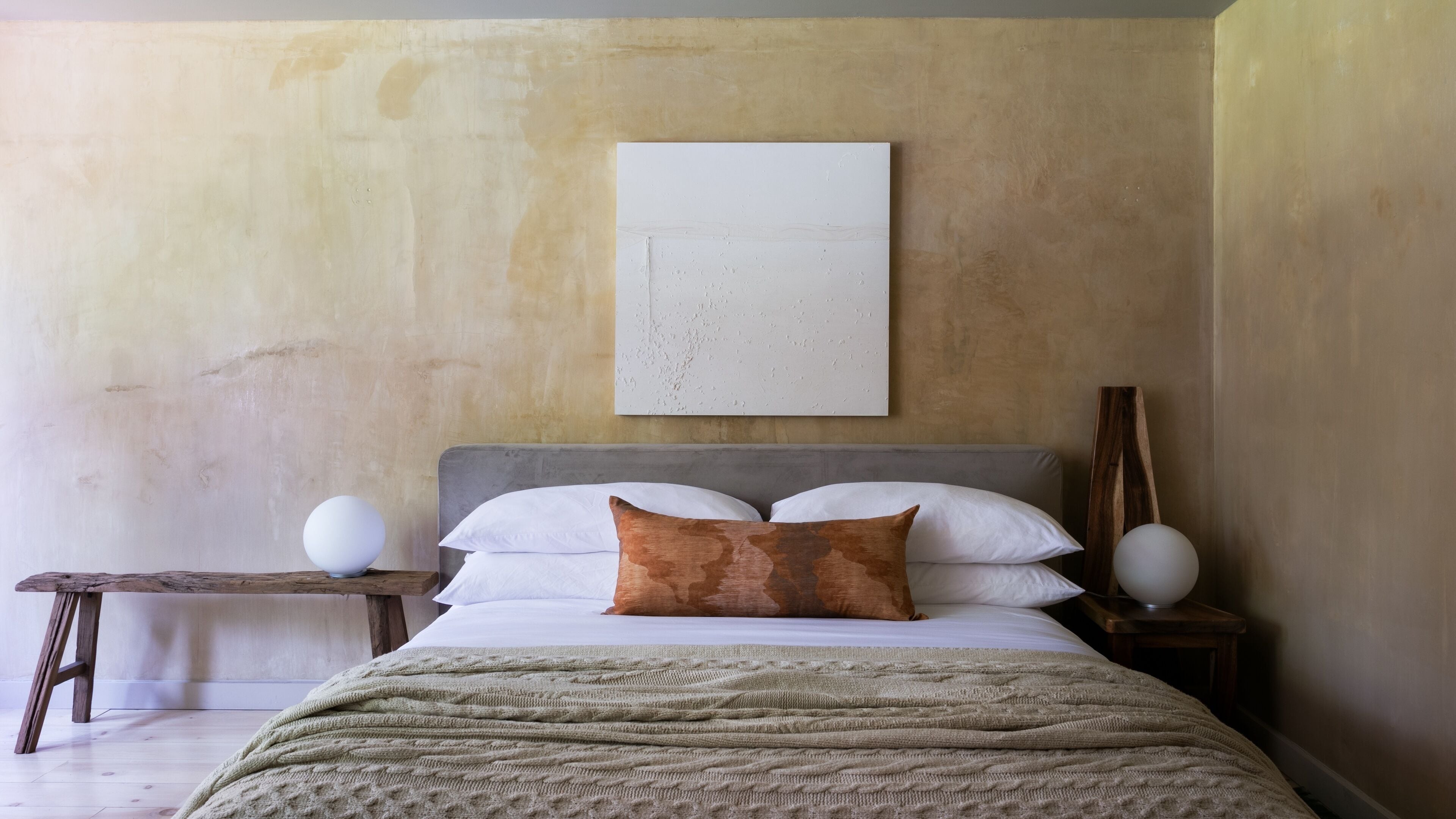 Une chambre à coucher avec un lit, une table de chevet avec une lampe et une œuvre d’art accrochée au mur.