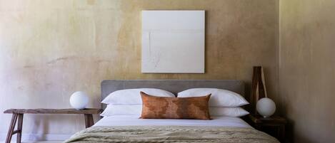 Une chambre à coucher avec un lit, une table de chevet avec une lampe et une œuvre d’art accrochée au mur.
