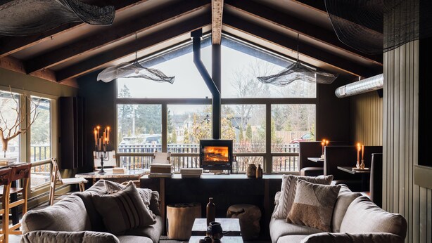 A cozy room with a fireplace, comfortable seating, and large windows offering a view of the outdoors. - AWOL Stowe (Stowe)