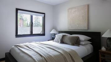 A bedroom with a bed, a nightstand, a lamp, a window, and a painting on the wall.