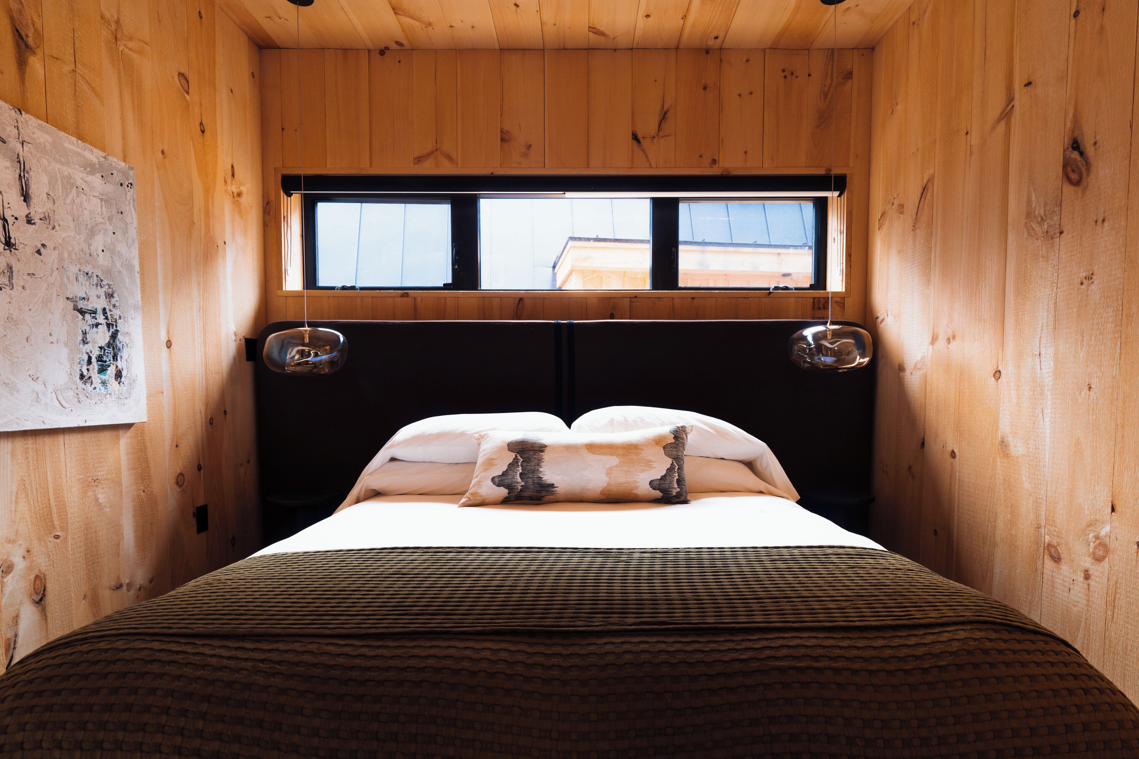 A wooden room with a bed, a window, and a wall-mounted artwork.