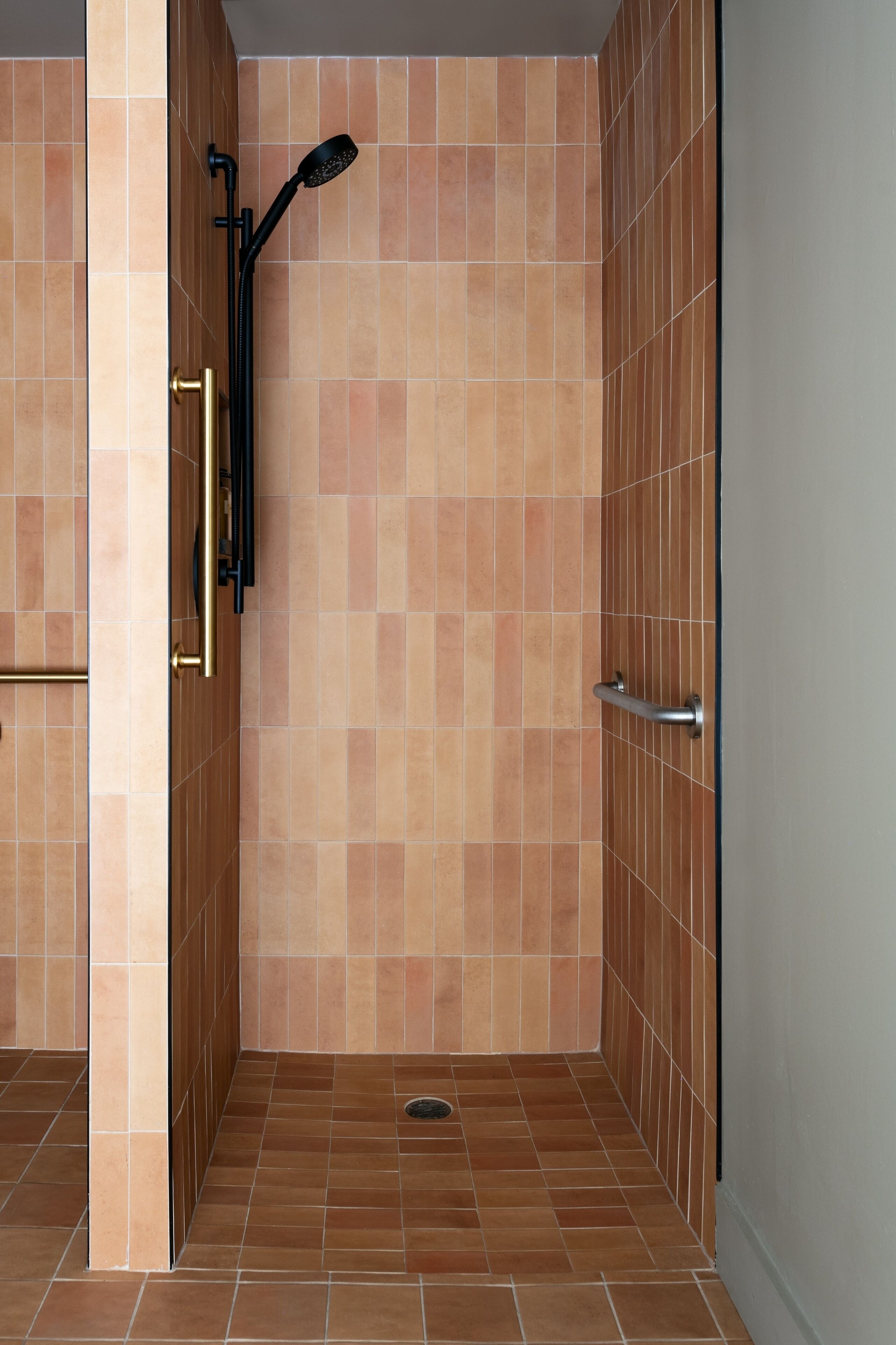 A walk-in shower with a tiled floor and walls, a handheld showerhead, and a metallic grab bar.