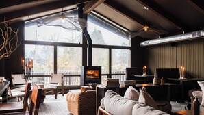 A cozy living room with a fireplace, large windows, and wooden furniture. - AWOL Stowe (Stowe)