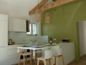 Una cocina moderna con armarios blancos, una mesa de comedor con sillas y lámparas colgantes de mimbre.