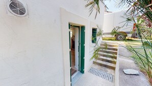 A narrow outdoor corridor with a metal vent on the wall, a green door, and a concrete staircase leading to a vehicle parked outside.