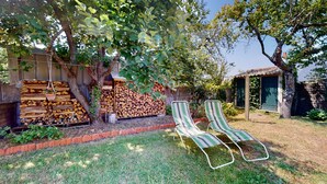 A backyard with a stack of firewood, two striped lawn chairs, and a small shed.