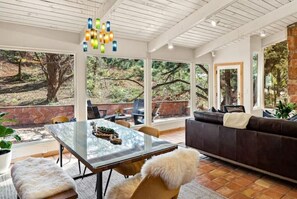 Enjoy a serene view of the wooded landscape from the comfort of this room, featuring a glass-top dining table and a cozy seating area.