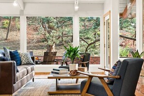 Relax in a serene space with a view of the wooded area, featuring a comfortable seating area with a sofa, armchair, and coffee table.