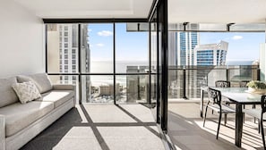 A modern apartment with a balcony, a sofa, and a dining area with a view of the city and ocean.