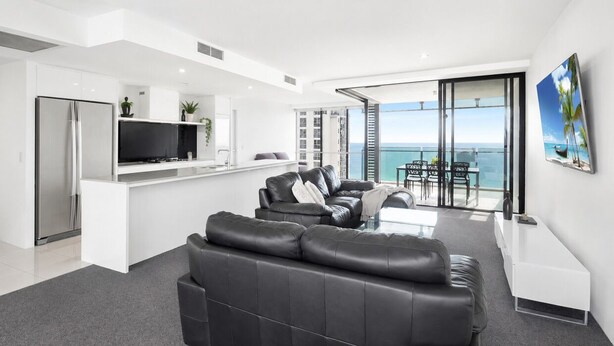 Ein modernes Wohnzimmer mit einer schwarzen Ledersofa, einem Flachbildfernseher und einem Balkon mit Blick aufs Meer.