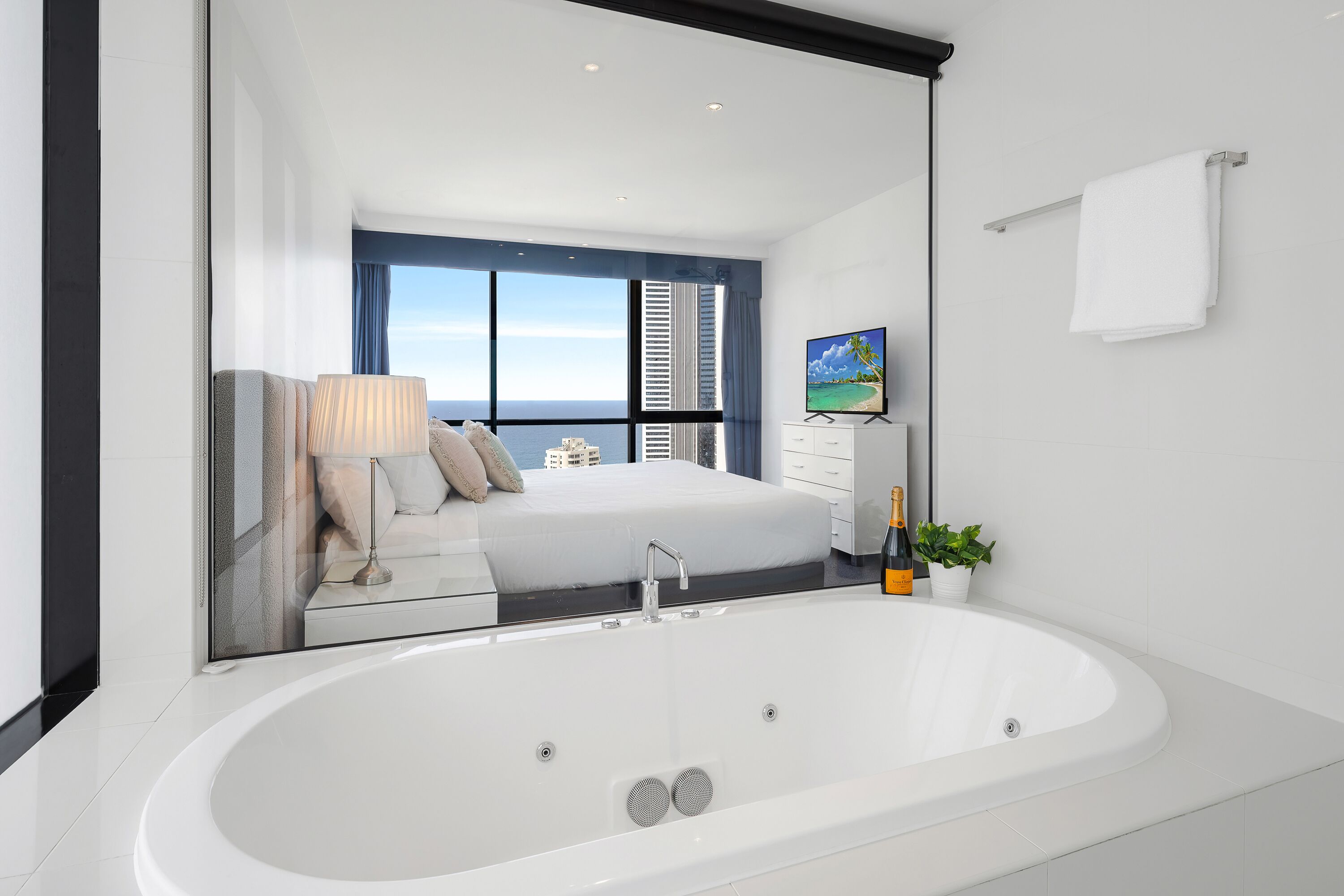 Una habitación de hotel moderna con una bañera grande, una cama con vistas a la ciudad, un televisor y una planta en maceta.