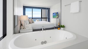 Ein modernes Hotelzimmer mit einer großen Badewanne, einem Bett mit Blick auf die Stadt, einem Fernseher und einer Zimmerpflanze.