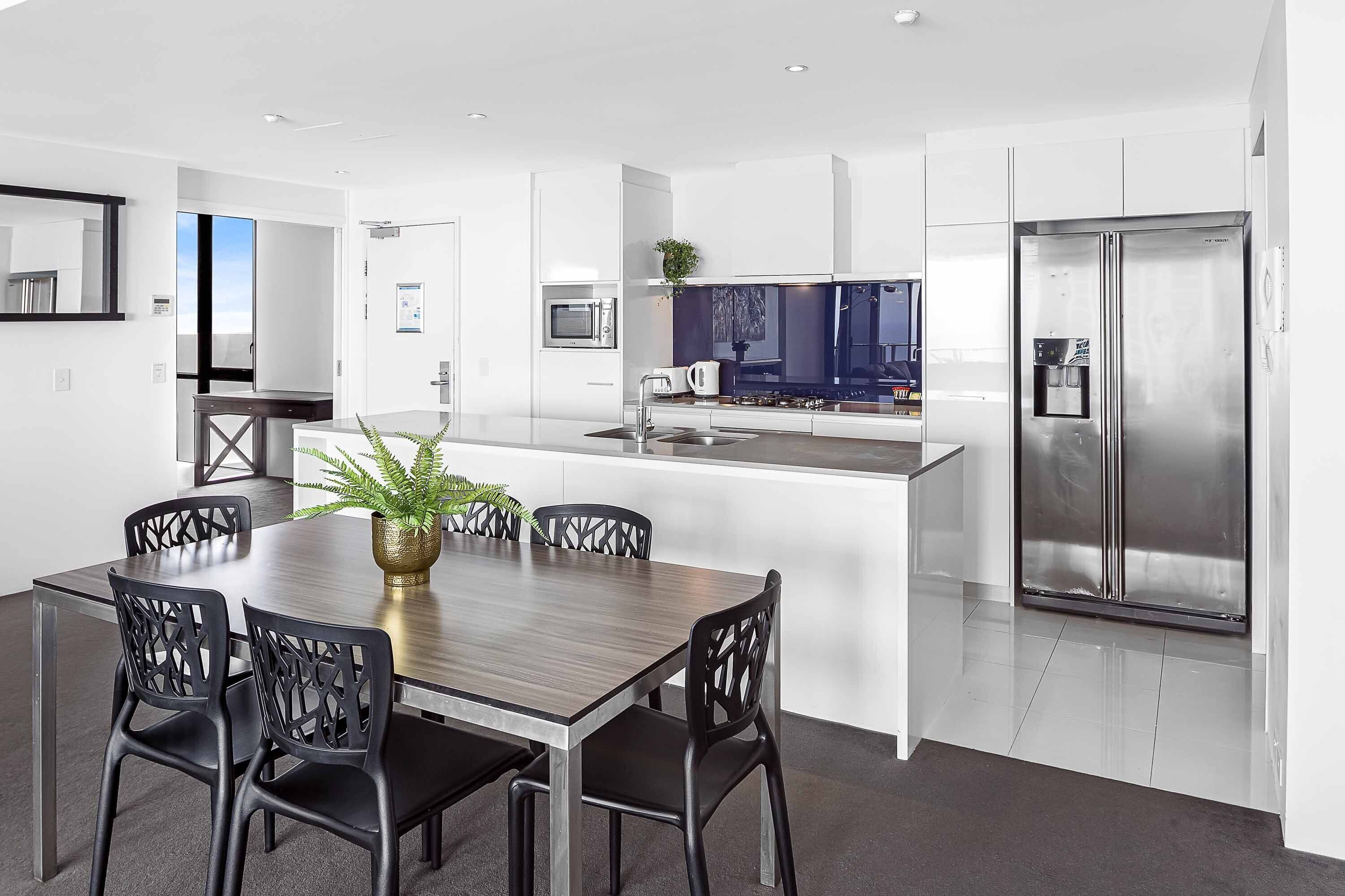 A modern kitchen with a central island, stainless steel appliances, and a dining area with a wooden table and black chairs.