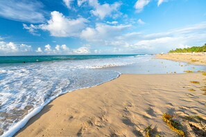 A beach with clear blue water, sandy shore, and distant palm trees. - Walking to Condado Beach and Near to Old San Juan (San Juan)