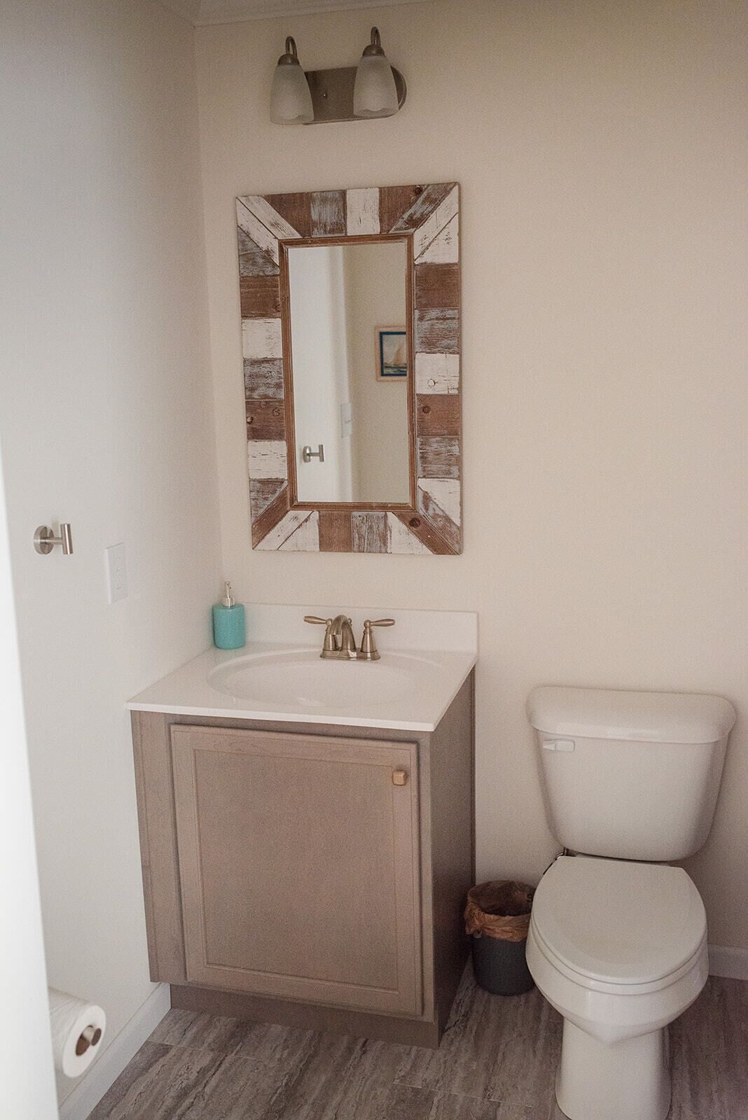 Une salle de bain avec un lavabo blanc, des toilettes et un miroir doté d’un cadre rustique.